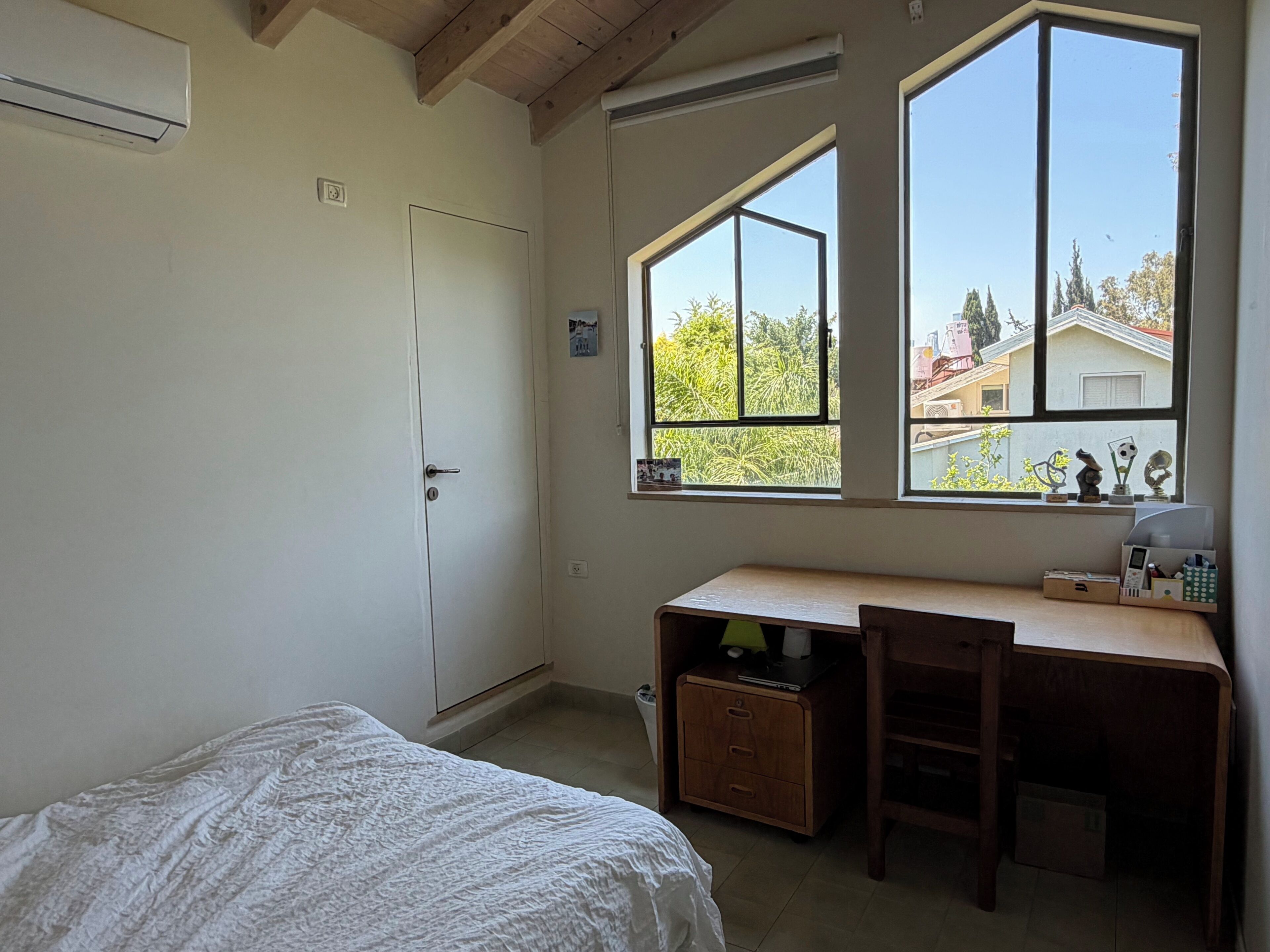 Quarto com cama, escrivaninha, cadeira e duas janelas.