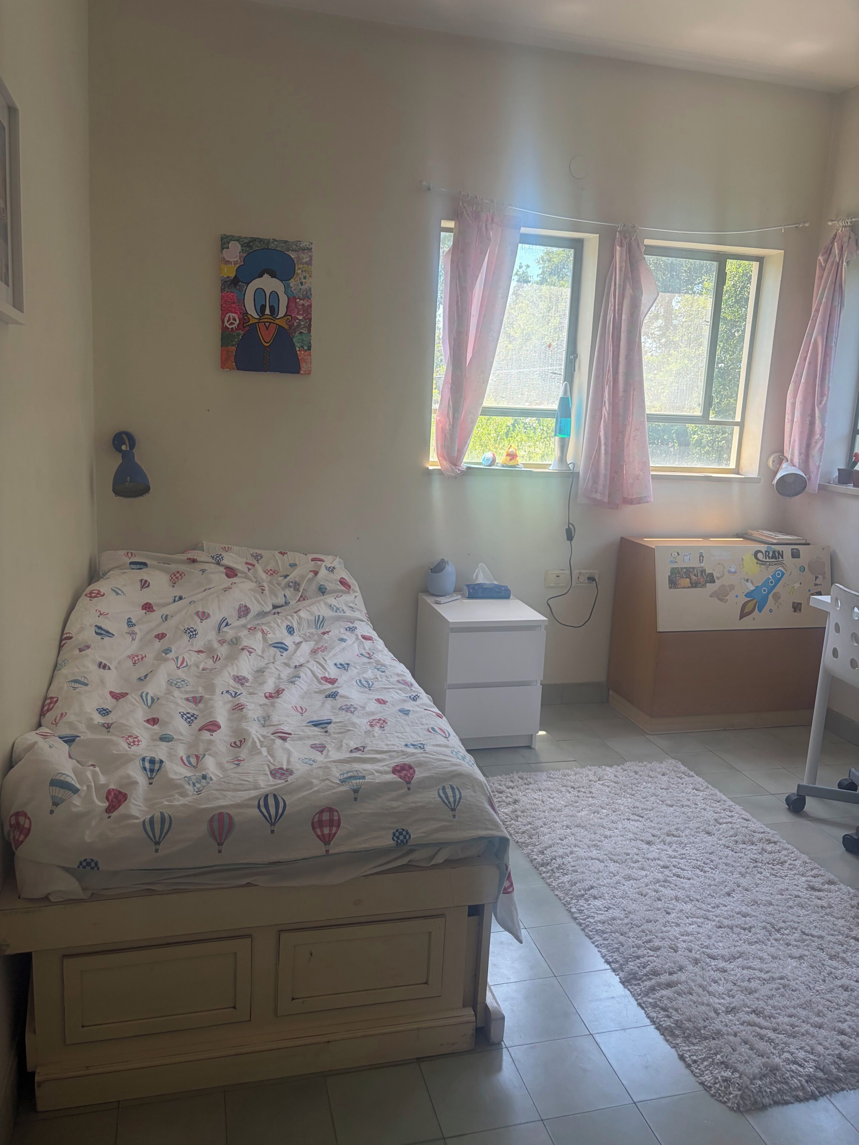 Un dormitorio con cama, mesita de noche y ventana con cortinas.