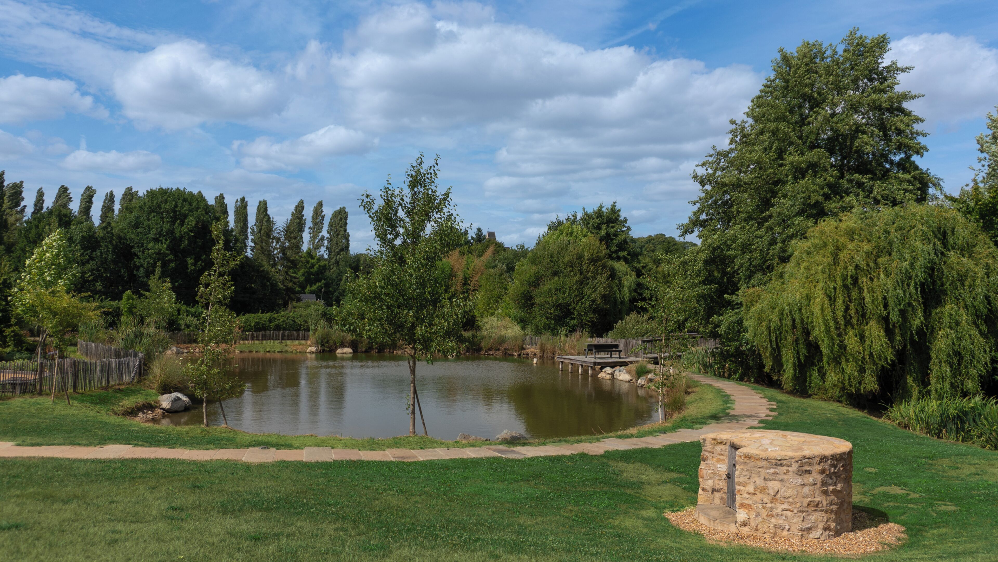 A serene park with a pond, a wooden bridge, and a stone structure.