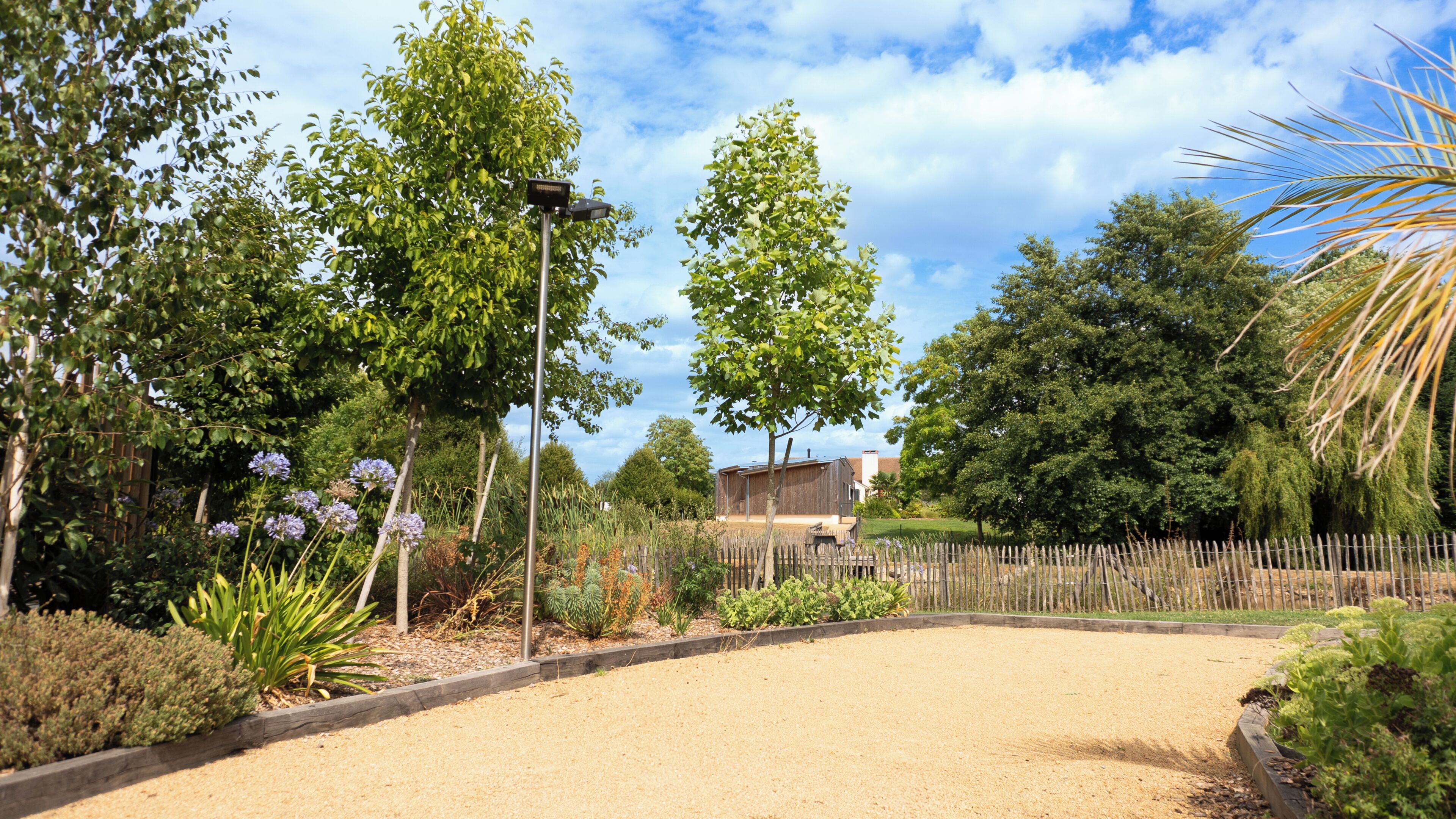A garden with a gravel path, various plants, and a wooden fence.