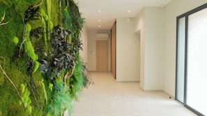 Un couloir avec un mur recouvert de mousse, une porte en bois et une grande fenĂȘtre.
