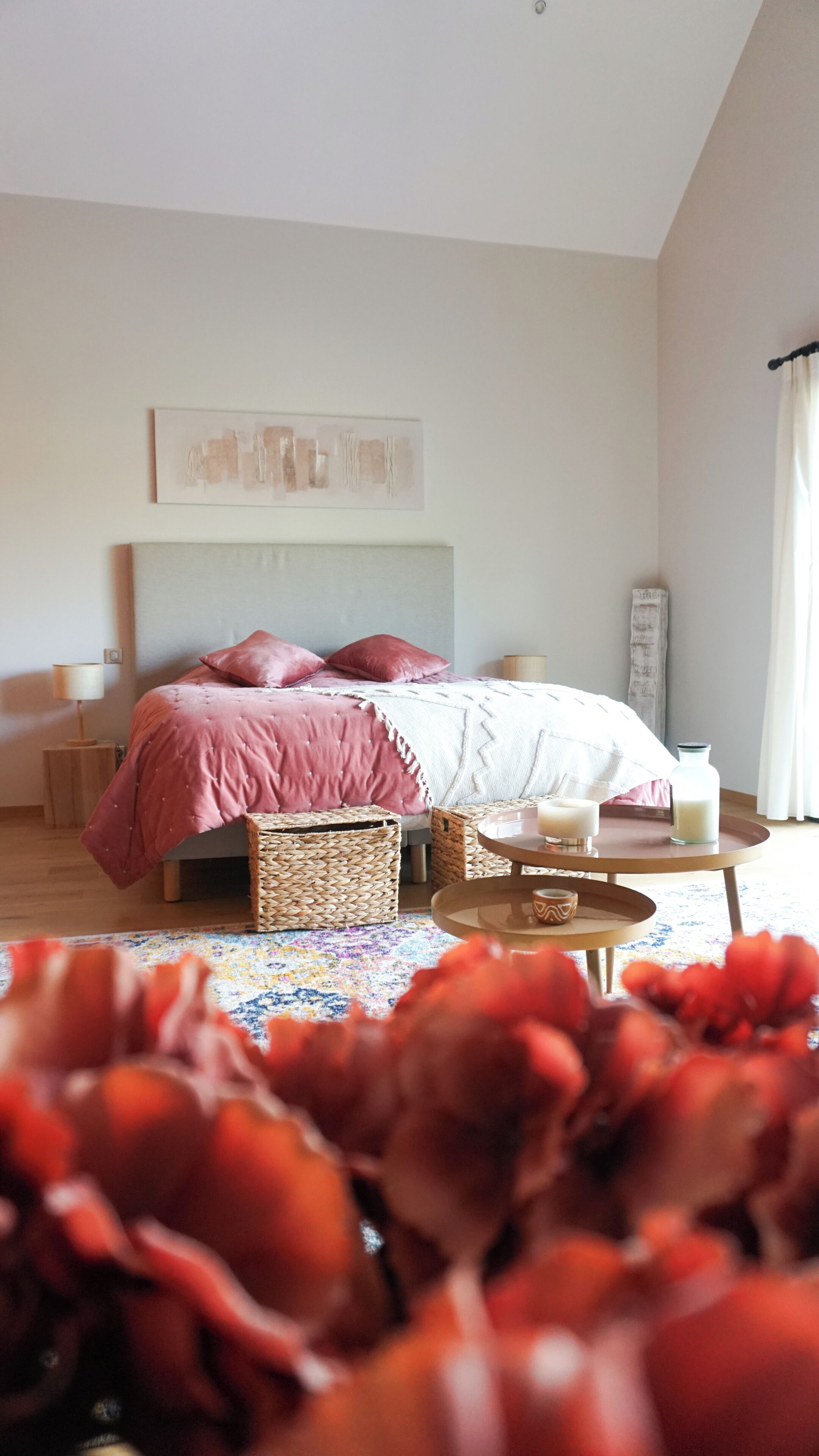 Ein Schlafzimmer mit Bett, Nachttischen, einer Lampe, einer Zimmerpflanze und einem Fenster mit Vorhängen.