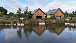 Eine Holzhütte mit Teich davor, umgeben von viel Grün.