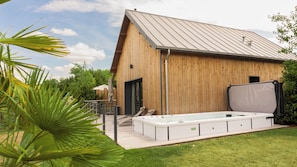 A modern wooden building with a metal roof, a hot tub, and a patio area.