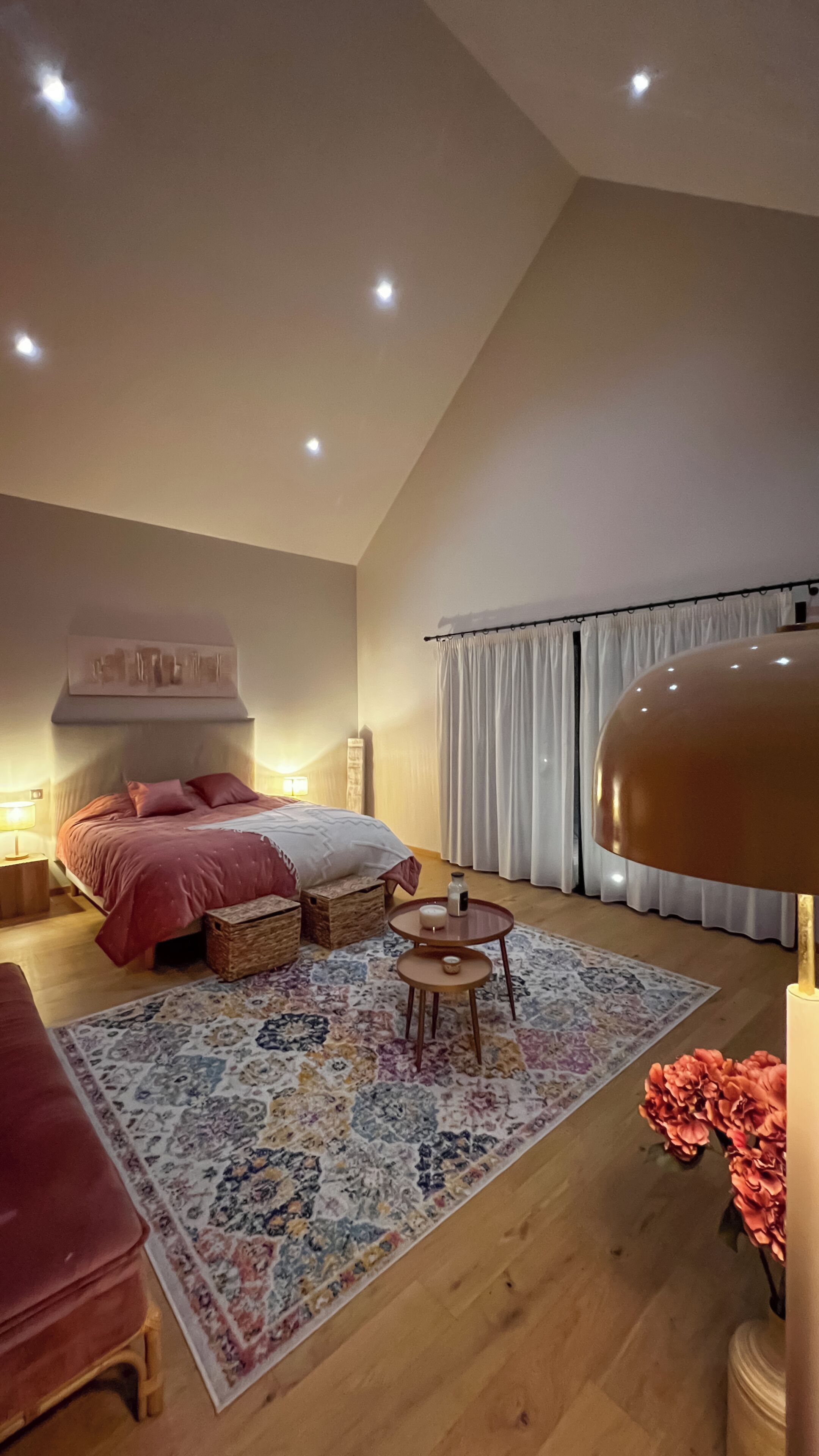 Ein Schlafzimmer mit einem Bett, Nachttischen, einer Lampe, einem Teppich und einem Fenster mit Vorhängen.