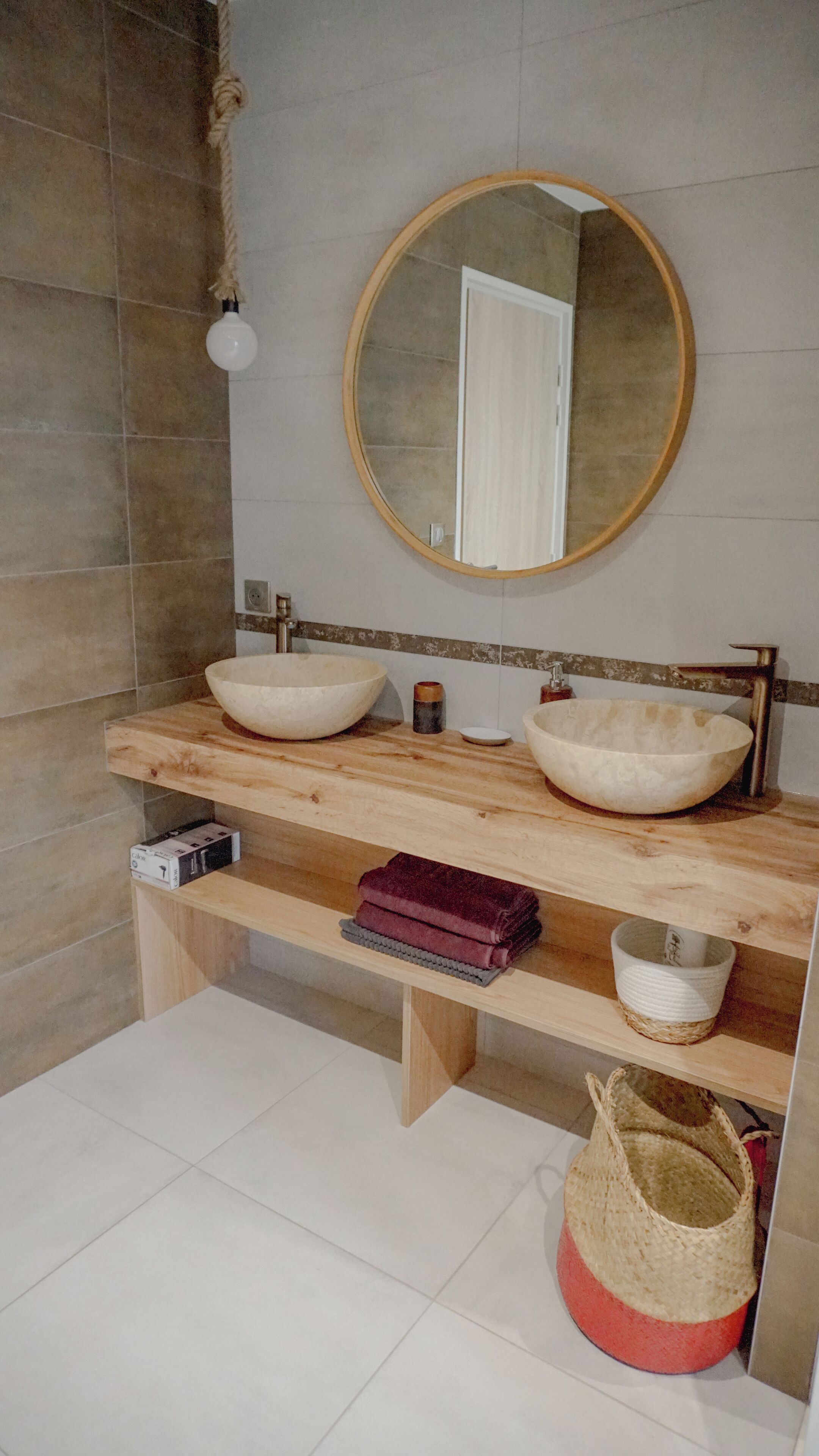 A bathroom with two large white vessel sinks, a round mirror, and a wooden vanity.