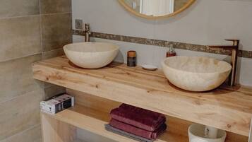 A bathroom with two large white vessel sinks, a round mirror, and a wooden vanity.