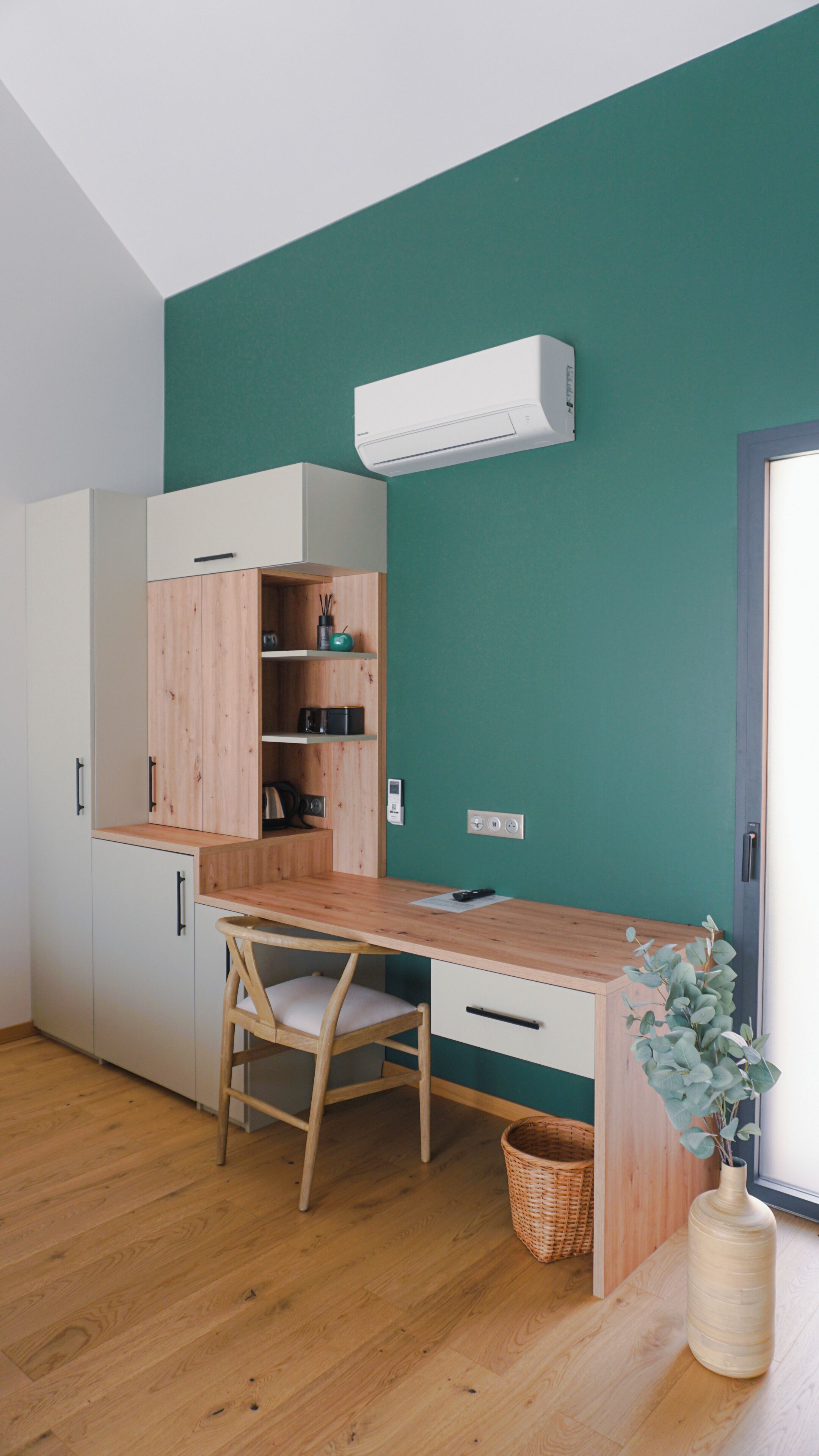 Une pièce avec un bureau en bois, une chaise, une armoire blanche, un mur de couleur turquoise et une fenêtre.