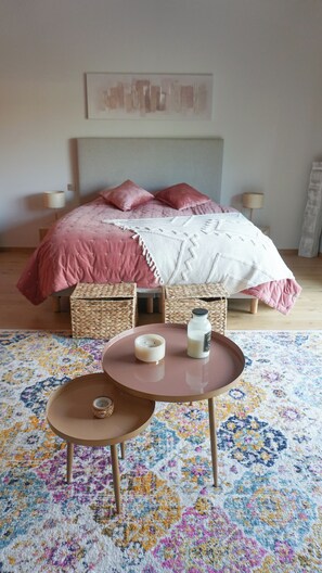 A bedroom with a bed, bedside lamps, a bedside table with candles, and a patterned rug.
