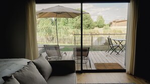 Ein Zimmer mit einem Bett, einer Couch, einer Schiebetür zu einer Terrasse mit Tisch, Stühlen und einem Sonnenschirm.