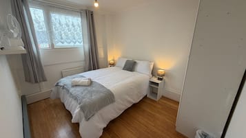 Une chambre à coucher avec un lit, des lampes de chevet, une fenêtre avec des rideaux, un luminaire au plafond et un plancher en bois.