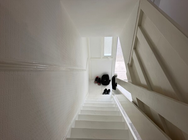 A white staircase with a handrail, leading to a landing where shoes and a backpack are placed. - Apartment Sleeps 6 - Wifi & Free Parking (Mitcham)