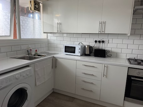 A modern kitchen with white cabinets, a built-in washing machine, a microwave, a toaster, and a gas stove.. Apartment Sleeps 6 - Wifi & Free Parking