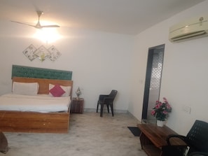 A bedroom with a bed, a desk, a chair, a ceiling fan, an air conditioner, and a wall-mounted light fixture.