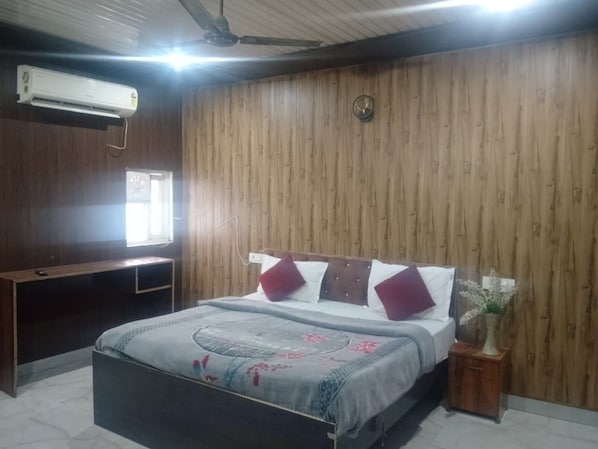 A bedroom with a bed, a desk, an air conditioner, and a wall clock.