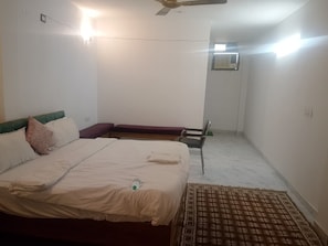 A bedroom with a bed, a chair, a ceiling fan, and an air conditioning unit.
