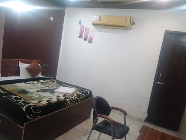 A bedroom with a bed, a chair, an air conditioner, and a door. - Govind Residency (Greater Noida)