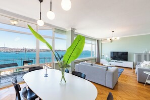 A modern living room with a large window, a dining area, and a sofa. - Azure Deluxe • Central Bosphorus View Flat (Beyoglu)
