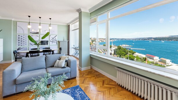 A modern living room with a sofa, dining table, and chairs, large windows with a city and sea view. - Azure Deluxe • Central Bosphorus View Flat (Beyoglu)