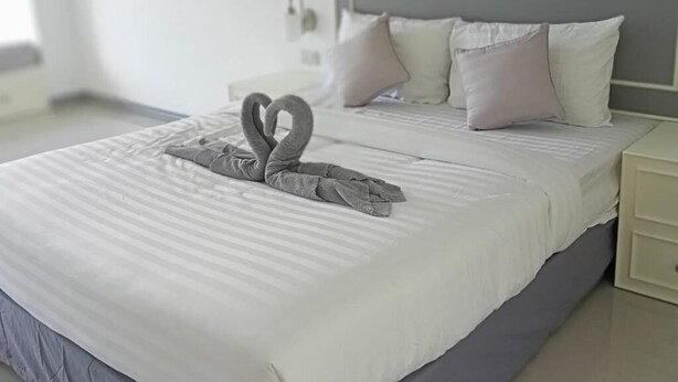 A neatly made bed with a towel arranged in a swan shape, a white headboard, and a bedside table with a lamp.