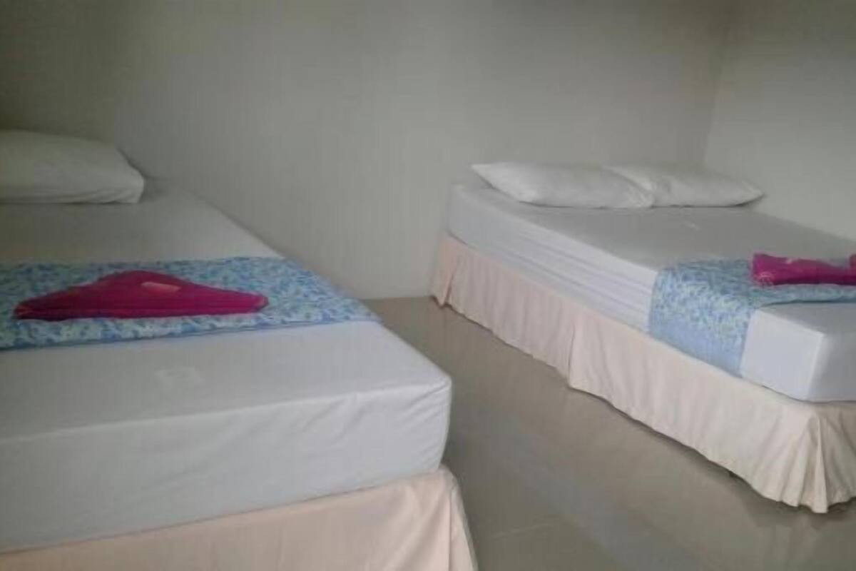 Two single beds with white mattresses and pink towels, a white wall, and a plain floor.