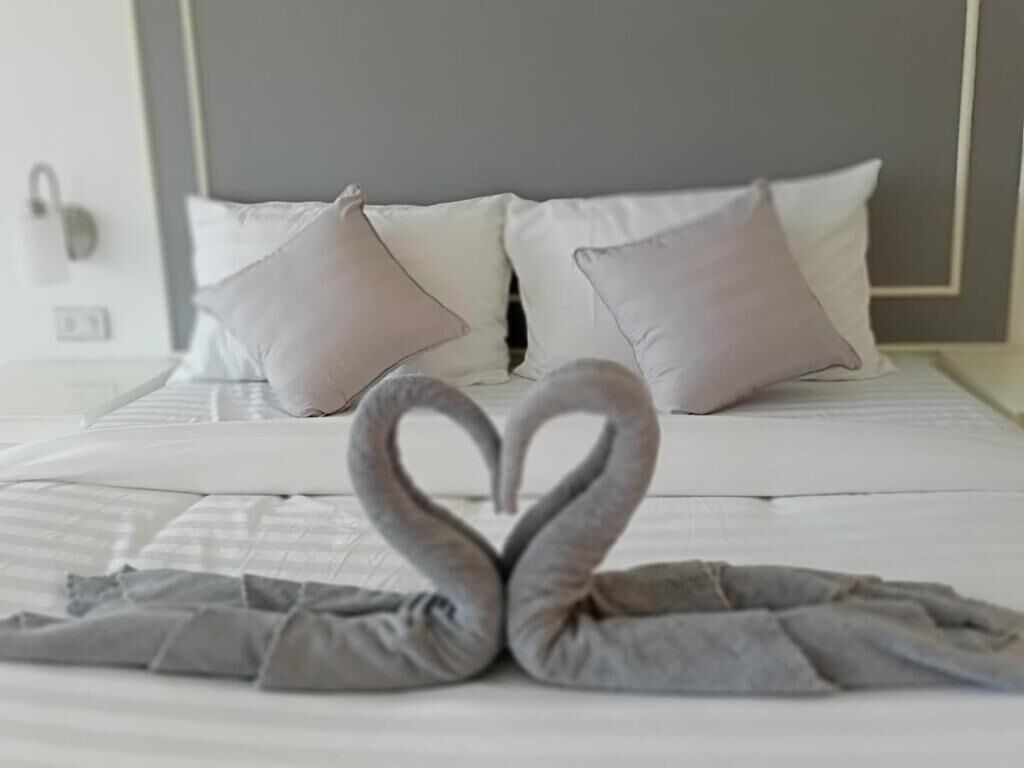A bed with a heart-shaped towel arrangement and a plain headboard.