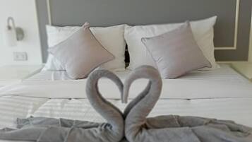 A bed with a heart-shaped towel arrangement and a plain headboard.