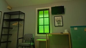 Una habitación con ventana, una silla, un escritorio, un televisor y un armario.
