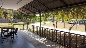 A covered outdoor area with a table and chairs, a railing, and a view of a residential street with trees and parked cars.