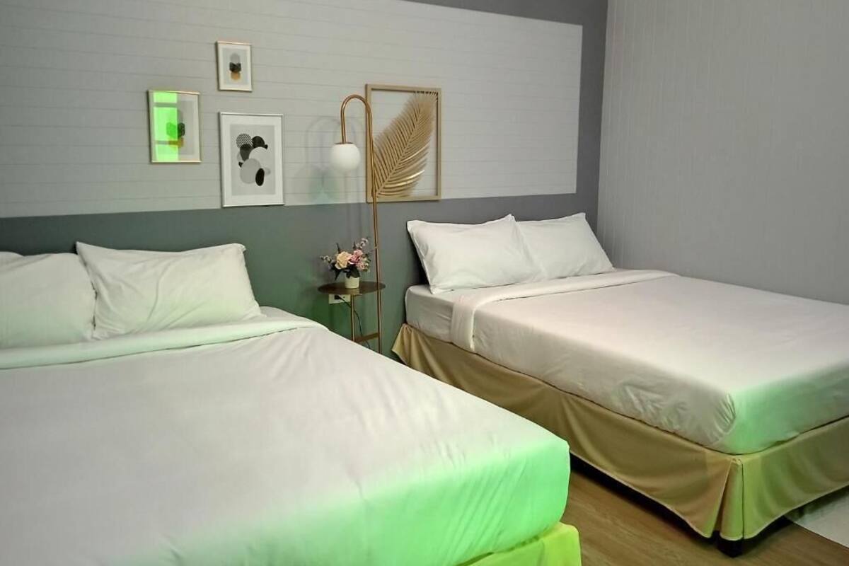 A hotel room with two beds, a nightstand with a lamp, framed artwork on the wall, and a small table with a vase.