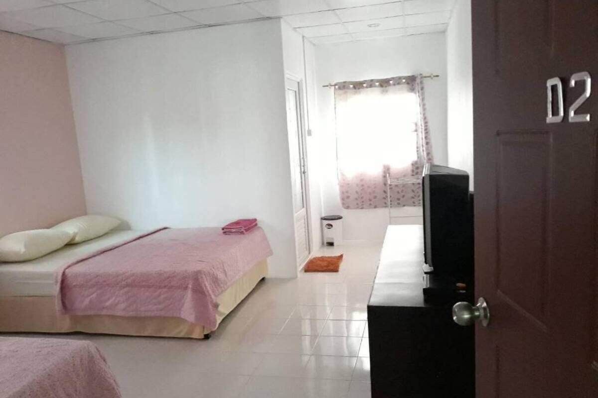 A bedroom with two beds, a television, a door with a number, and a window with curtains.