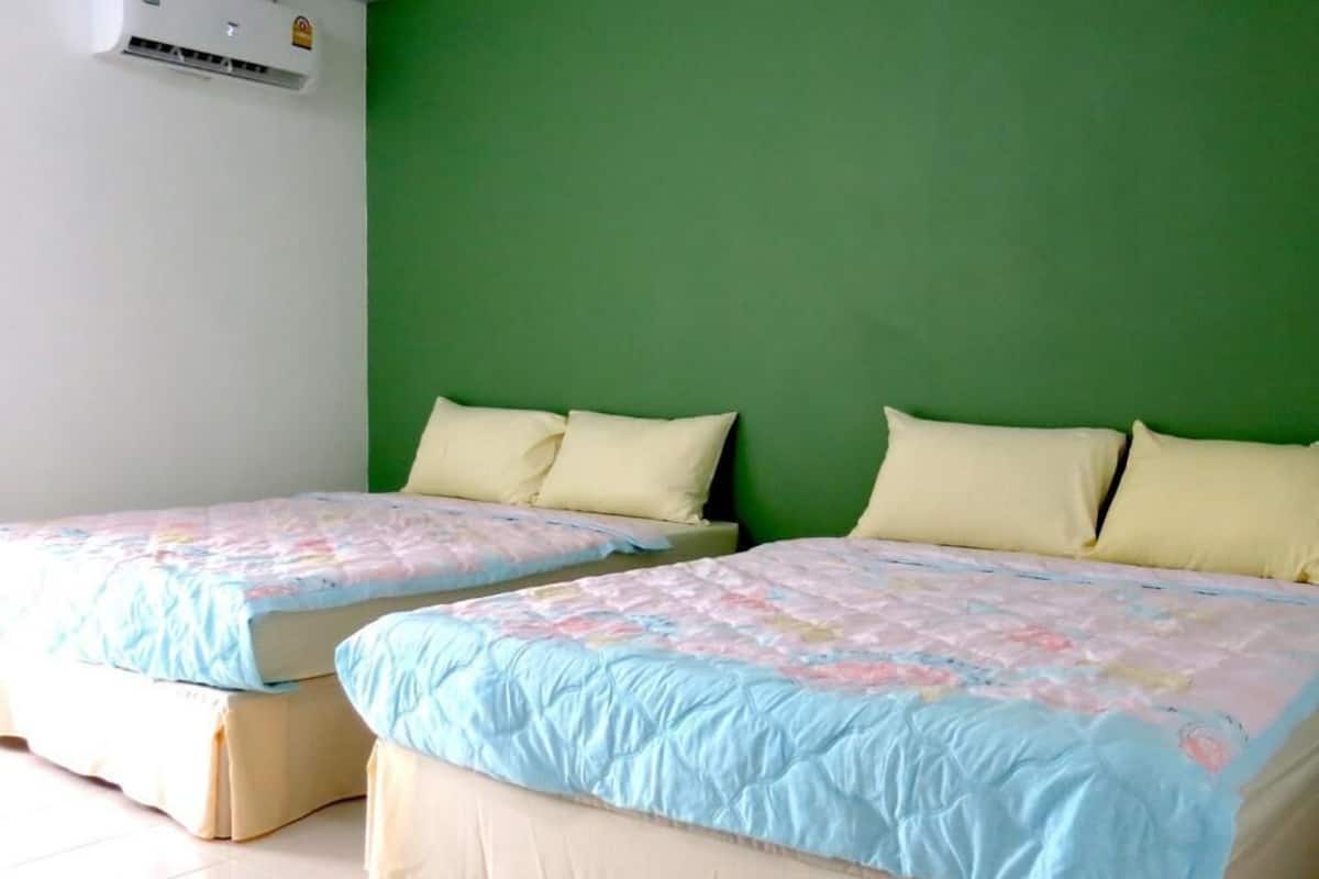 Two beds with matching bedding, a green wall, and an air conditioning unit.