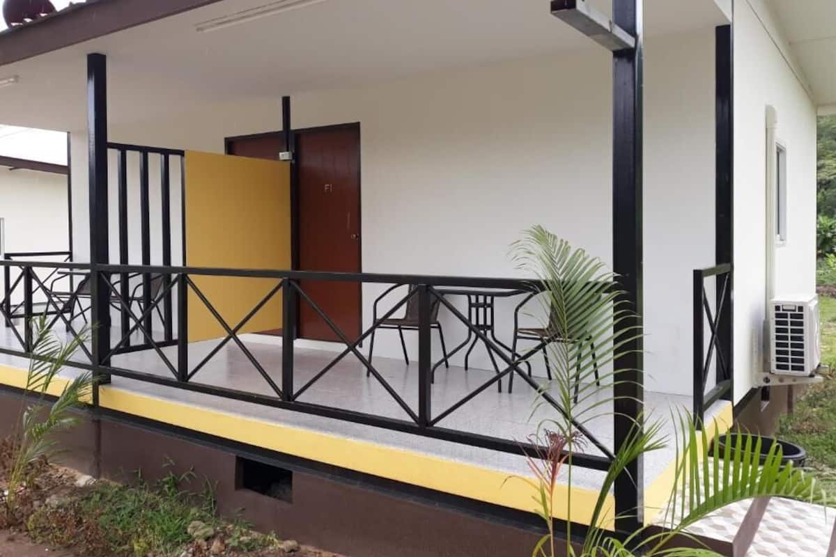 A covered outdoor area with a table and chairs, a door, and a small air conditioning unit.