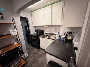A compact kitchen with white cabinets, a black stove, and a sink.