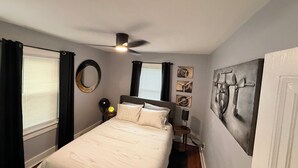 Un dormitorio con una cama, ventilador de techo, mesita de noche y obras de arte en las paredes.