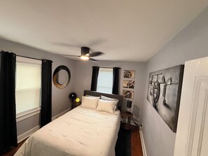 Une chambre à coucher avec un lit, un ventilateur de plafond, une table de chevet et des œuvres d’art accrochées aux murs.