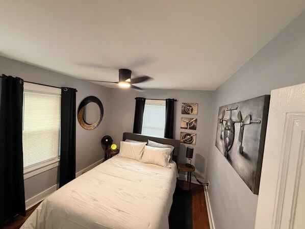 A bedroom with a bed, a ceiling fan, a bedside table, and artwork on the walls.