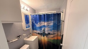 Un baño con inodoro, lavamanos y cortina de ducha con diseño de paisaje.