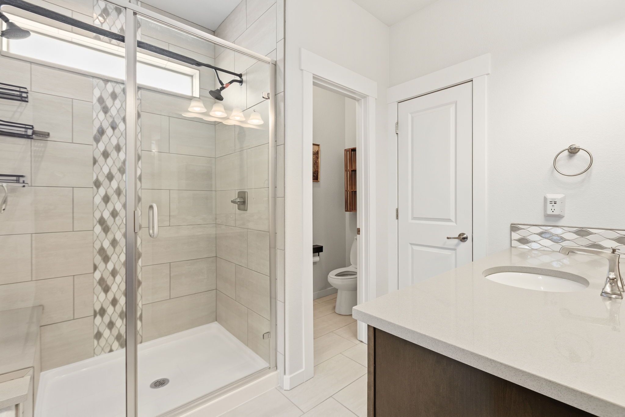 A modern bathroom with a glass-enclosed shower, a white sink, and a toilet.