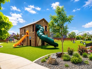 Une aire de jeux avec un toboggan, une structure d’escalade et un bâtiment à la façade en bois.