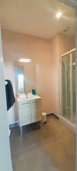 Ein Badezimmer mit einem weißen Waschtisch, einem Spiegel, einem Handtuchhalter und einer Glasdusche.