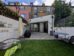 Ein Garten mit Terrasse, Grill, Gartenmöbeln und einem weißen Zaun.