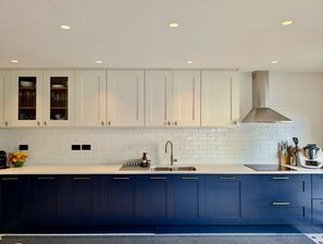 Eine moderne Küche mit weißen Oberschränken, einem blauen Unterschrank, einer Edelstahlspüle und einer Dunstabzugshaube.