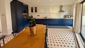 Een moderne keuken met donkerblauwe kastjes, een centraal eiland en een eethoek met een tafel en stoelen.