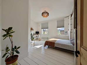 A bedroom with a bed, a desk, and a chair, a potted plant, and a window. - Chic Property With Backyard Near Emirates Stadium (London)