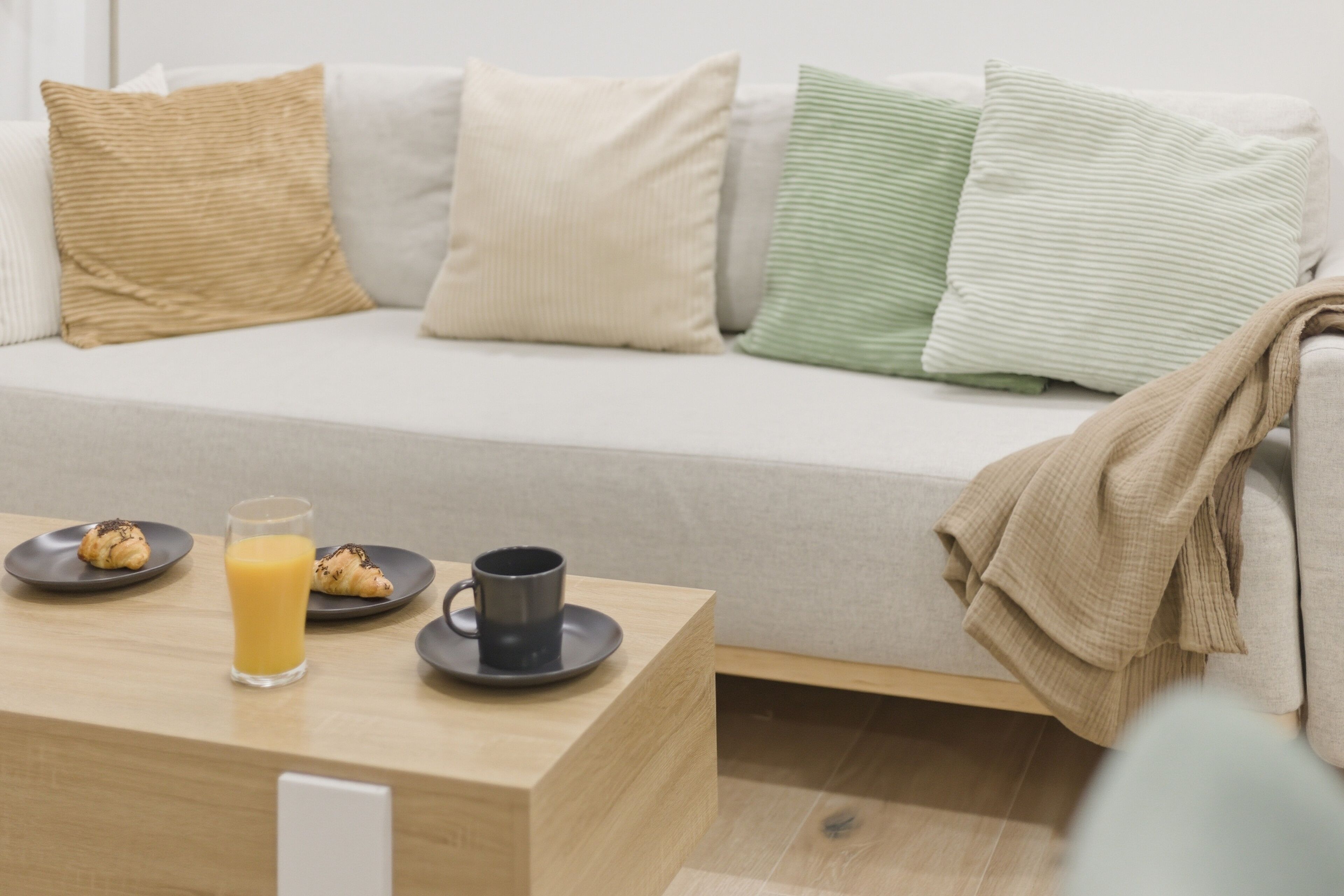 A modern living room with a sofa, cushions, a coffee table, and a breakfast setup with croissants and juice.