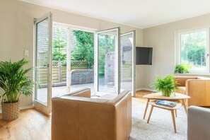 Ein Wohnzimmer mit einer Schiebetür zum Patio, einem Sofa, einem Couchtisch und einem an der Wand befestigten Fernseher.