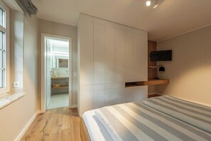 Ein Schlafzimmer mit Bett, Fernseher, integriertem Kleiderschrank und angrenzendem Badezimmer.