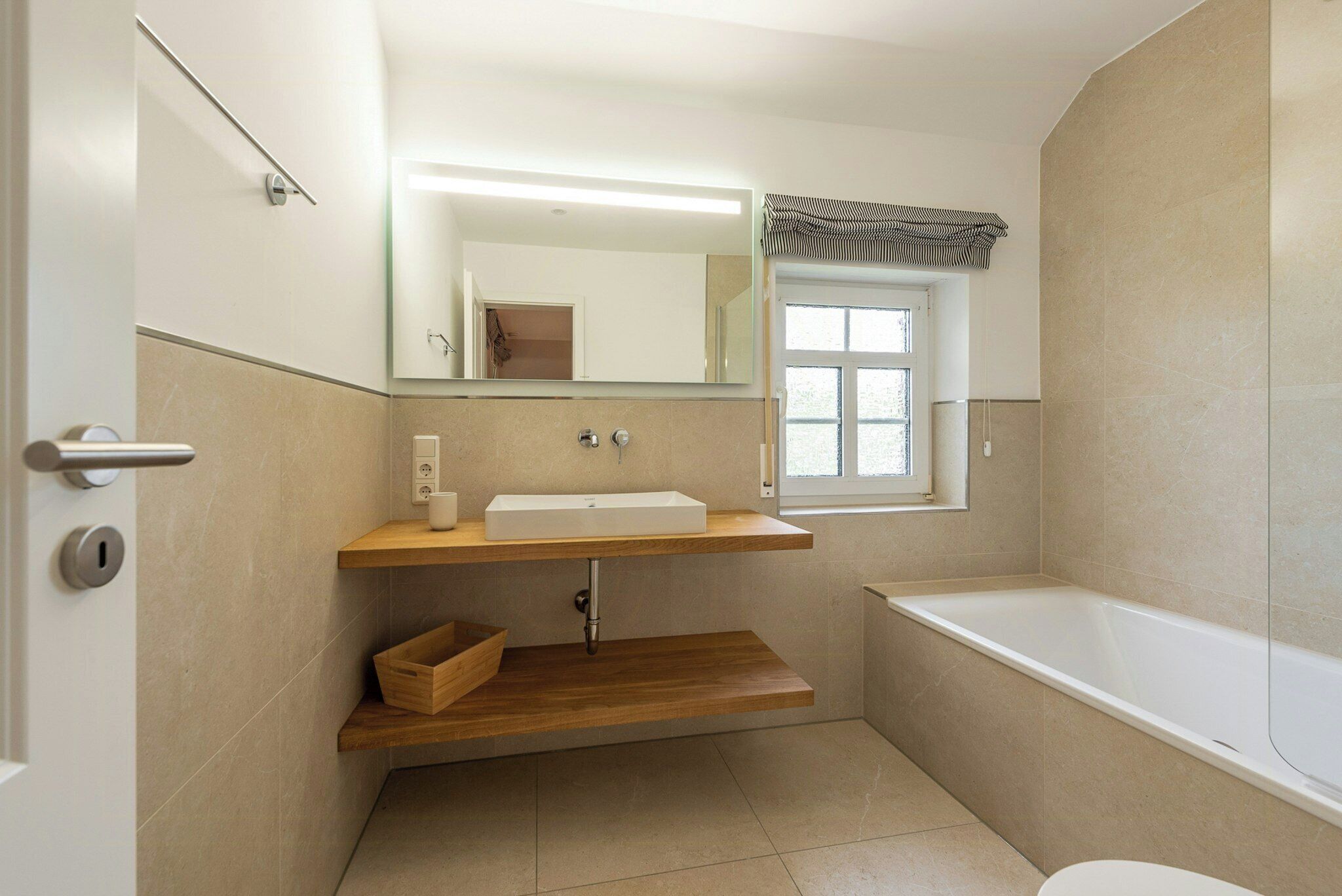 Ein Badezimmer mit Waschbecken, Spiegel, Fenster, Badewanne und einem Holzregal.