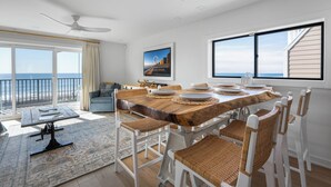 Ein Essbereich mit Holztisch, weißen Stühlen und Blick auf das Meer.